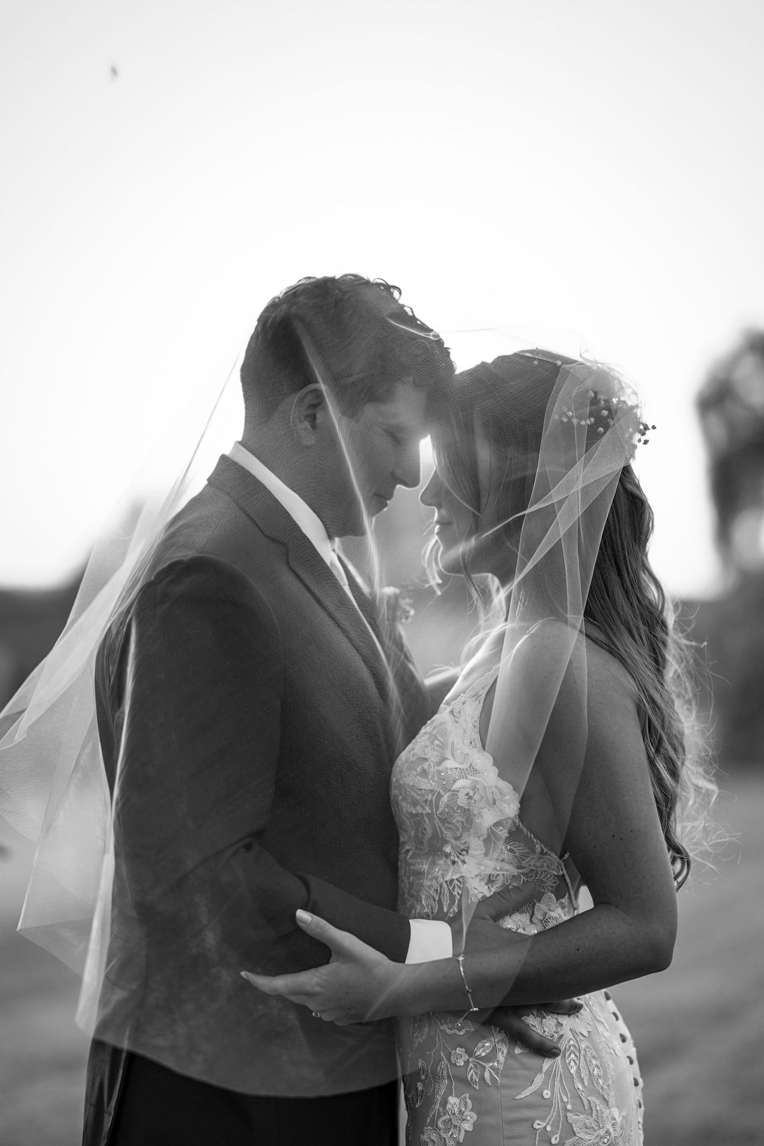 A romantic black and white wedding photo series showing a couple in an intimate embrace under a flowing veil.