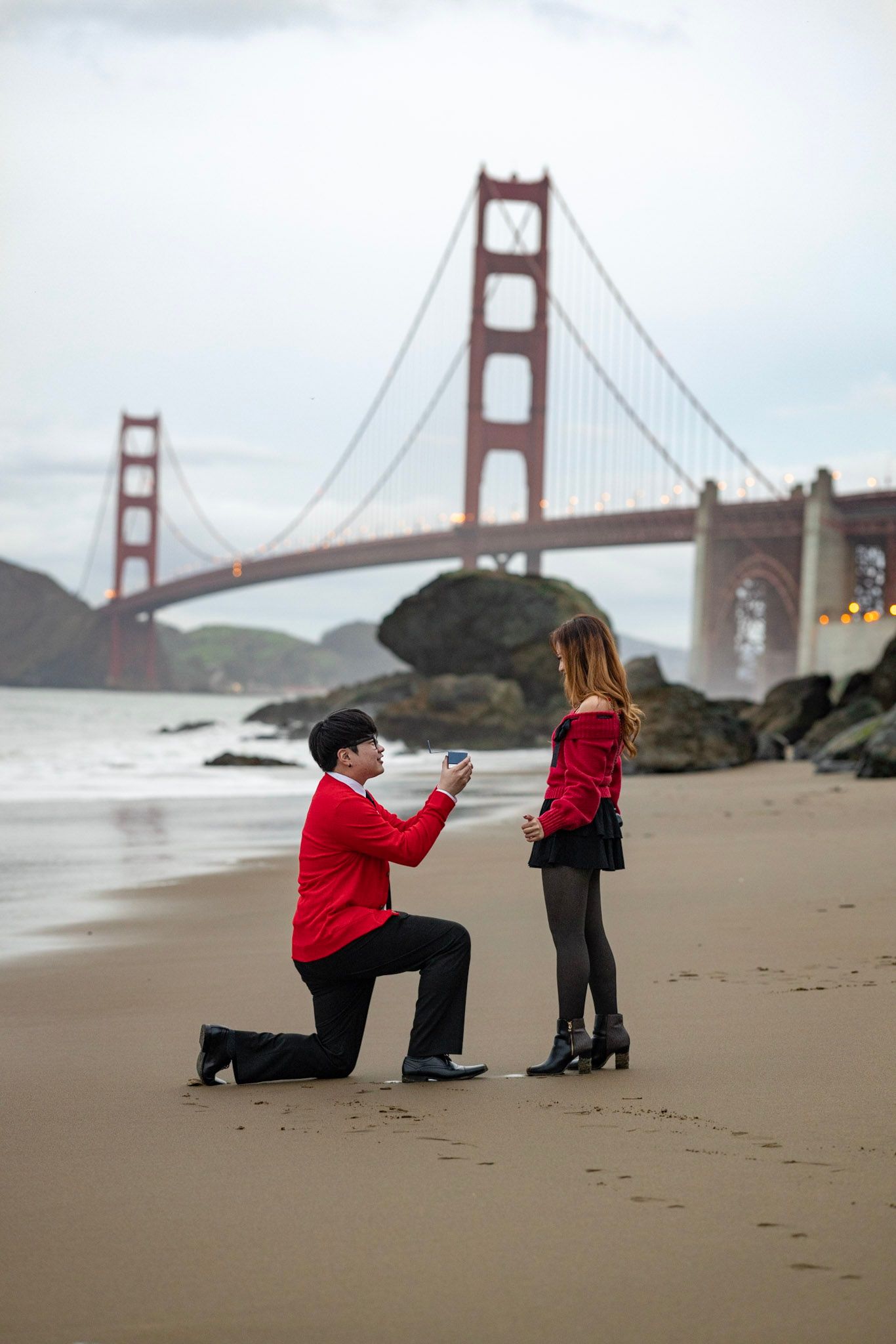 A marriage proposal scene unfolds on Baker Beach with the iconic Golden Gate Bridge in the background.