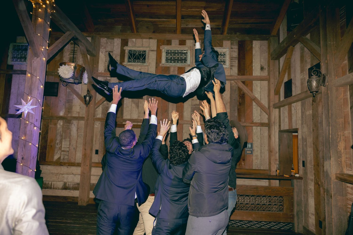 A group of dancers perform a choreographed routine in a rustic barn setting with dramatic lighting.