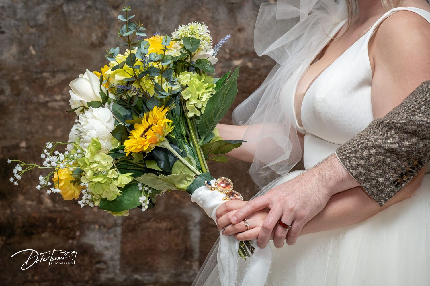 Close-up of hands holding a vibrant yellow and white wedding bouquet against rustic brown background.