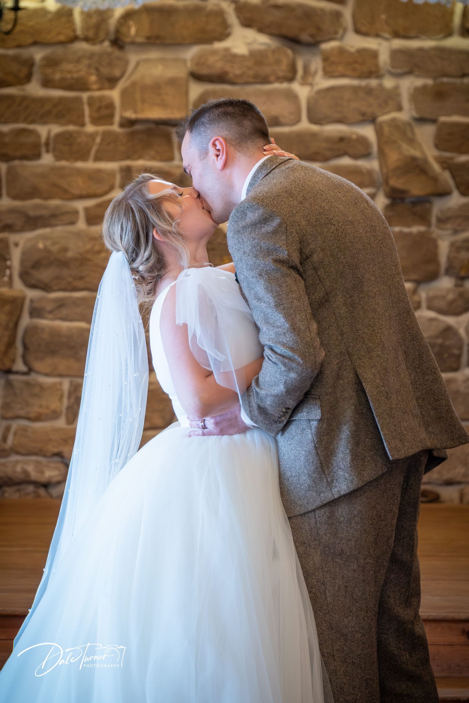 A romantic wedding moment between newlyweds in front of a rustic stone wall.