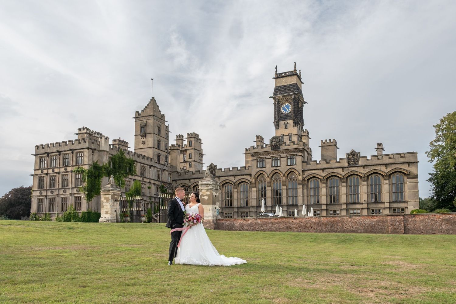 Panoramic view of historic stone castle and grounds with wedding couple in distance.