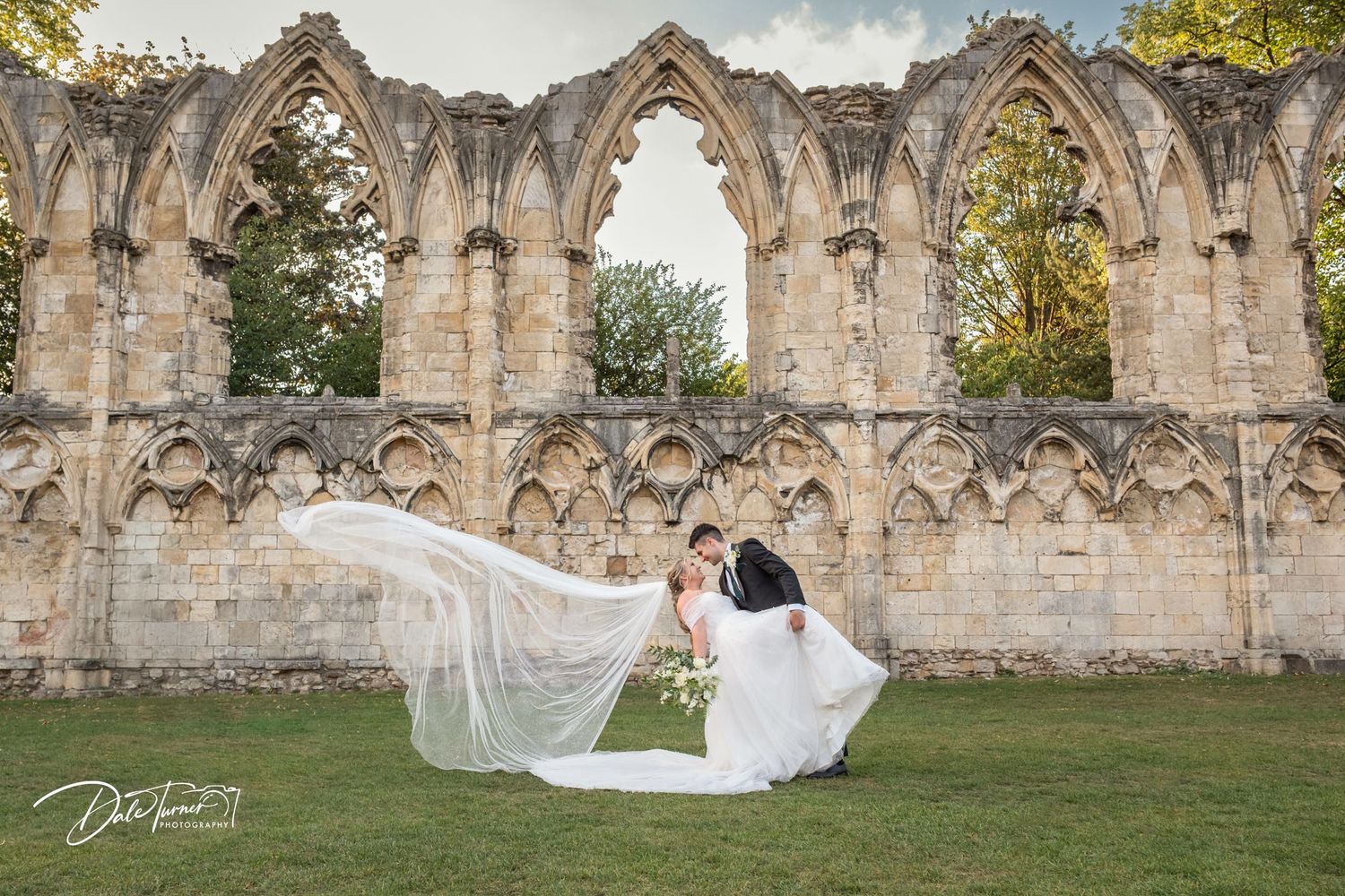 A flowing veil creates dramatic movement against gothic ruins during a wedding photoshoot.