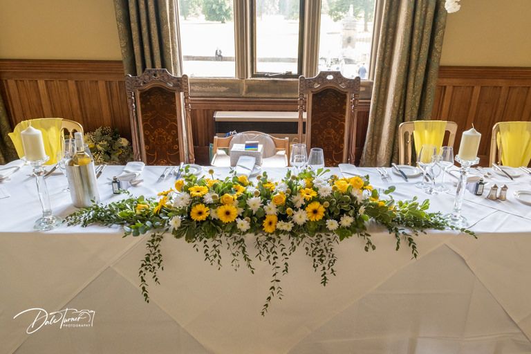 Wedding reception tables decorated with yellow floral arrangements and formal place settings.