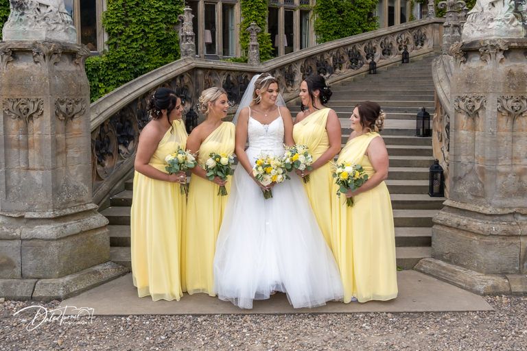 Wedding party in yellow dresses posing on stone steps of historic building.