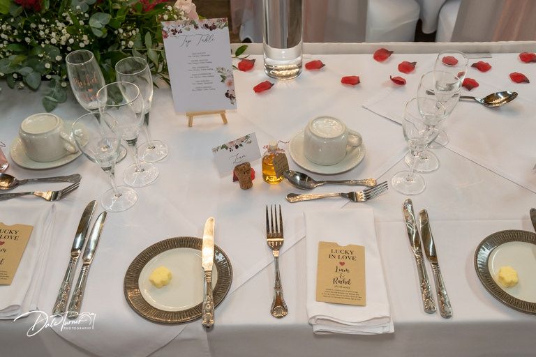 Formal wedding table settings with white linens, rose petals, and wooden slice centerpieces.