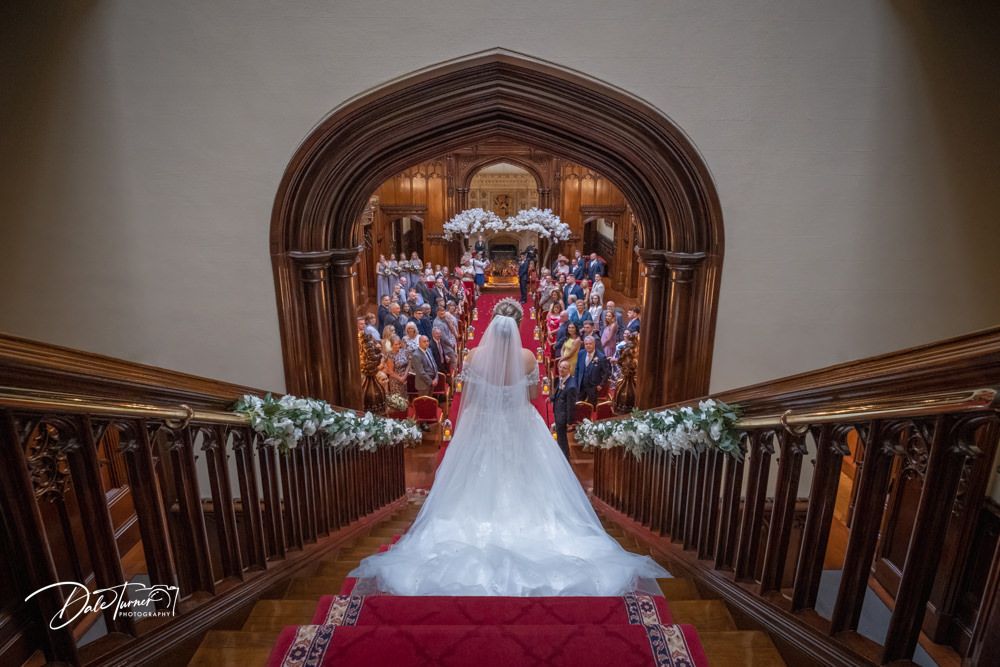 Long wooden corridor with red carpet leading to ornate Gothic archway.