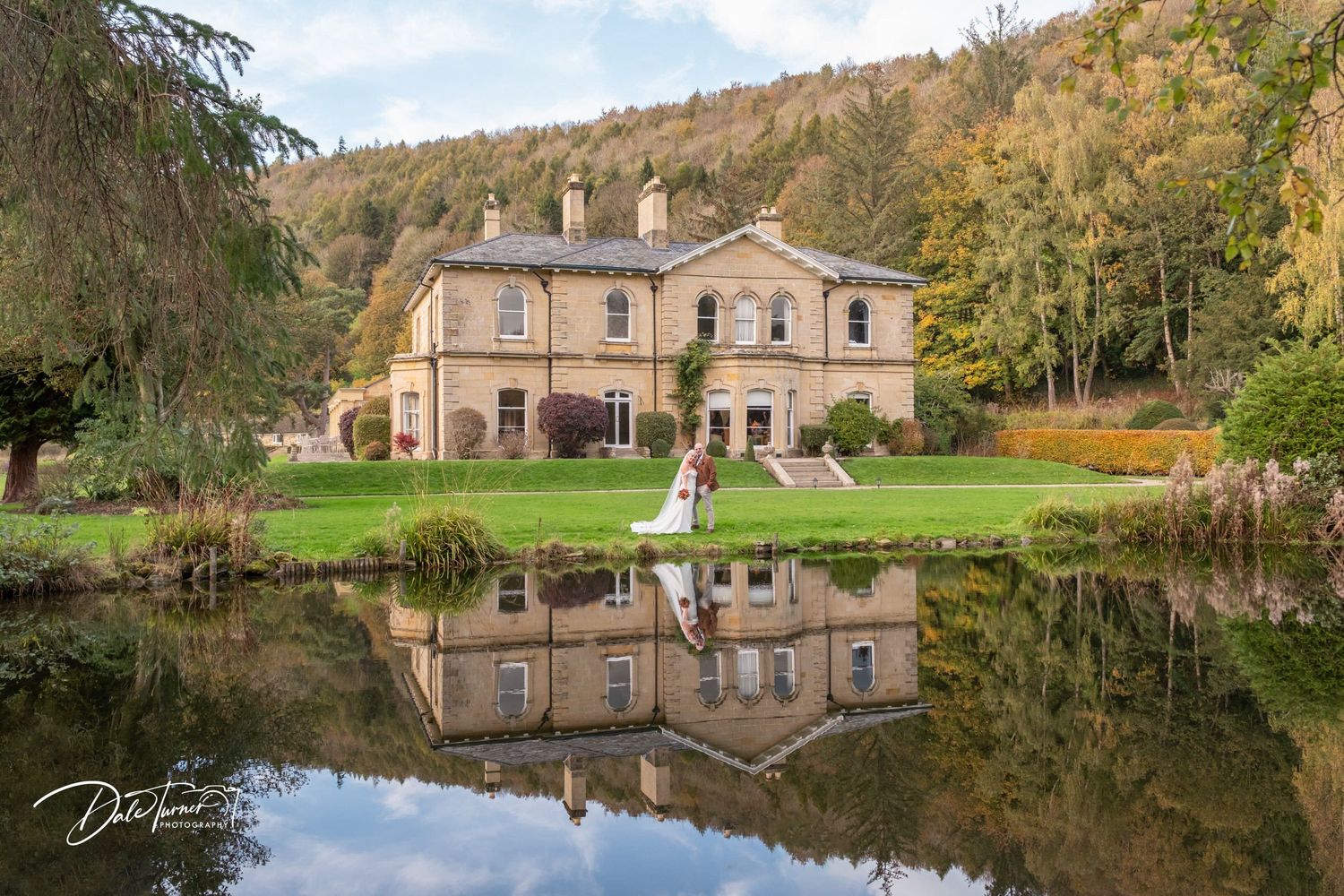 Historic stone building reflected in calm lake waters surrounded by autumn foliage.
