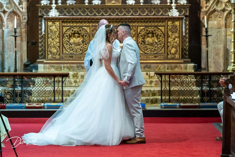 Wedding couple at ornate golden altar in majestic cathedral setting.