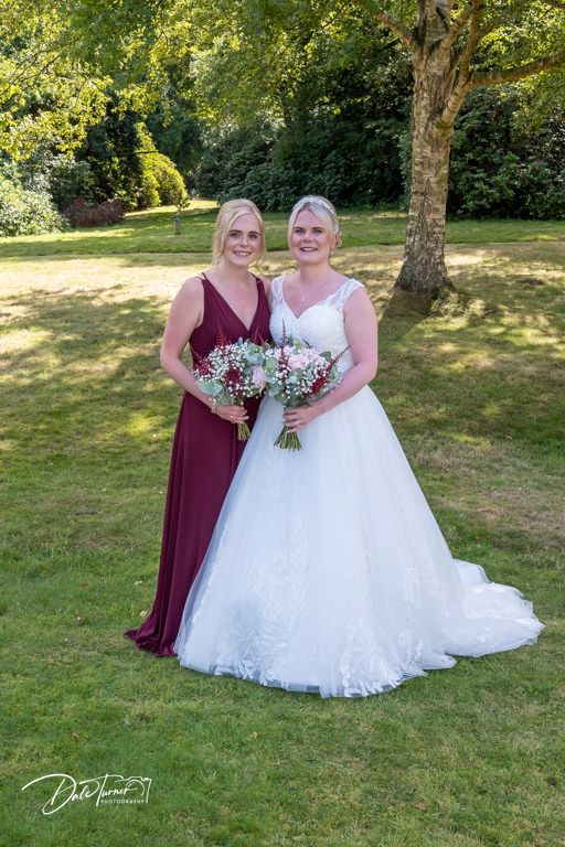Wedding party poses in a sunny garden setting with burgundy and white dresses and floral bouquets.