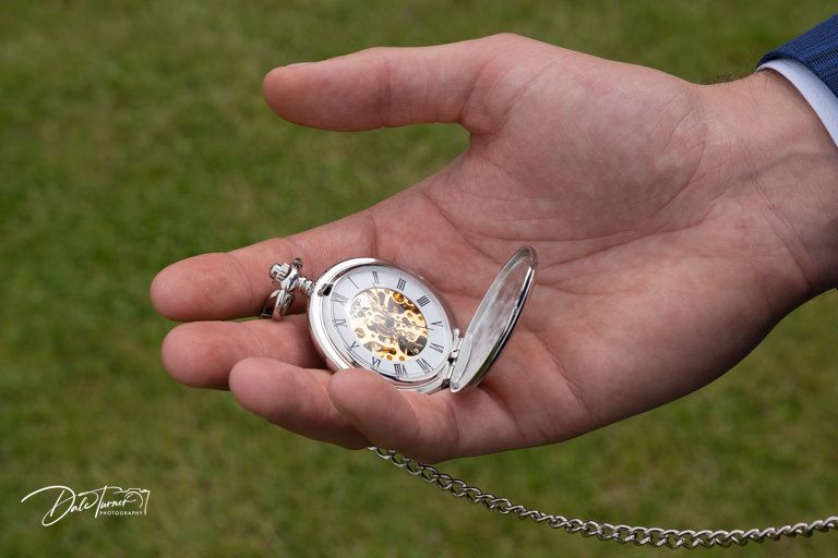 Close-up of hands holding delicate vintage pocket watch on grassy background.