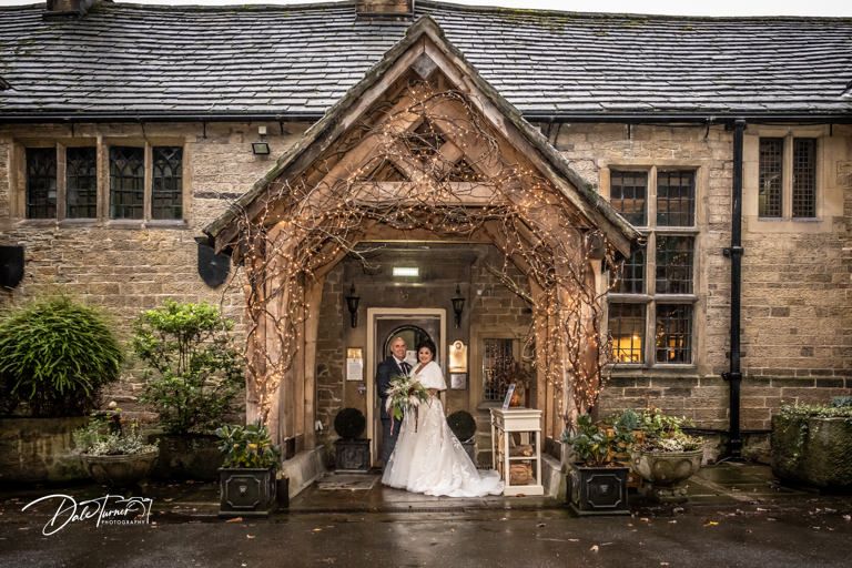 Wedding portrait under stone archway entrance of historic building in the rain.