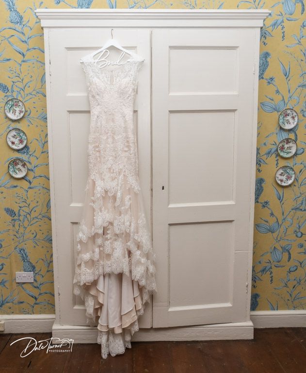 Wedding dress hanging on white doors against yellow floral wallpaper.