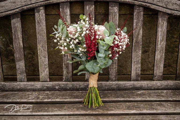 Wedding bouquet with red and white flowers rests on rustic wooden bench.