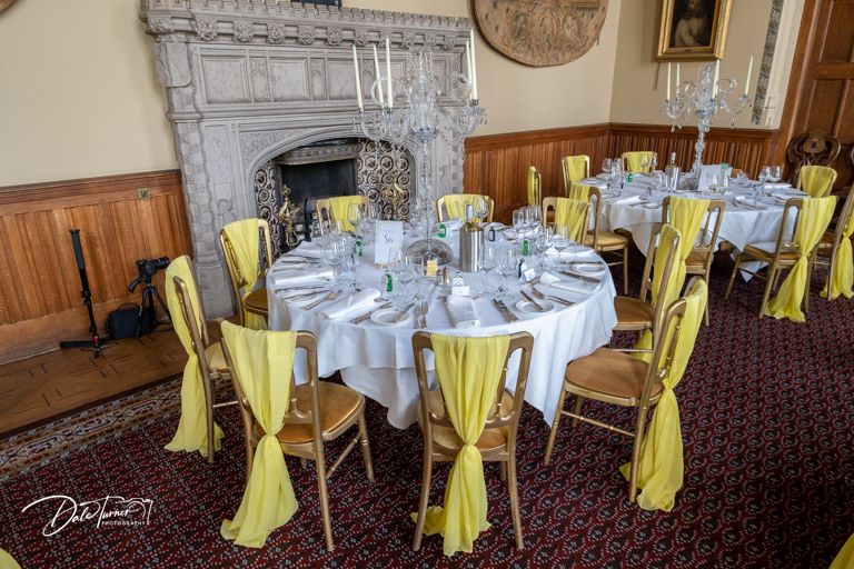 Elegant wedding reception venue with round tables decorated with yellow accents and white linens.