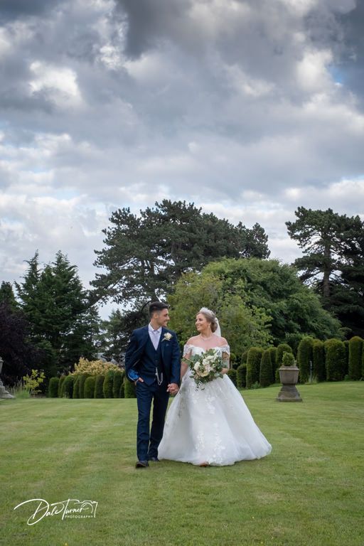 A romantic wedding couple poses on a lush green lawn under dramatic cloudy skies.