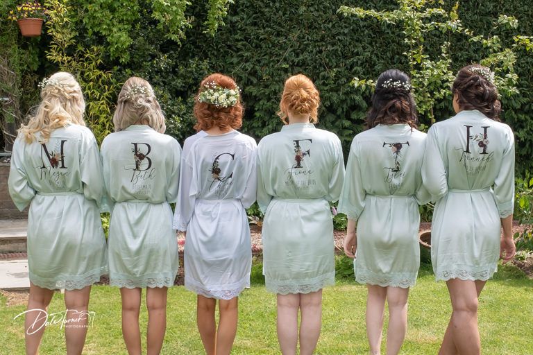 Bridesmaids wearing matching mint robes show off embroidered details from behind.