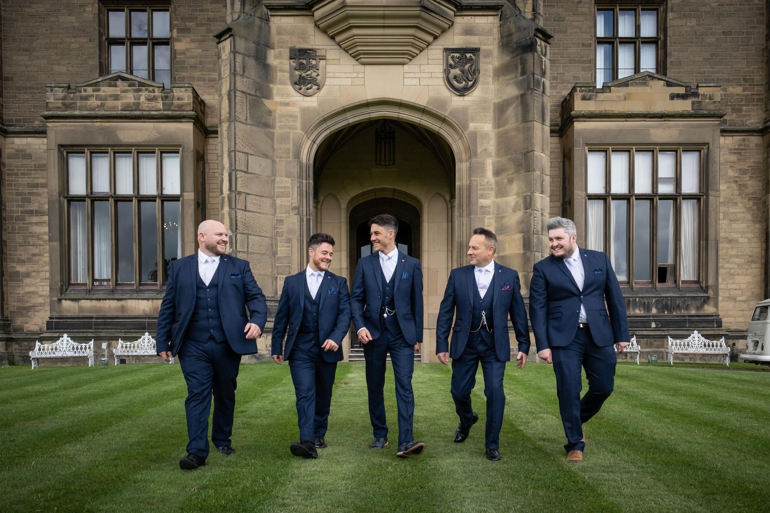 Groomsmen in navy suits walking across castle grounds.