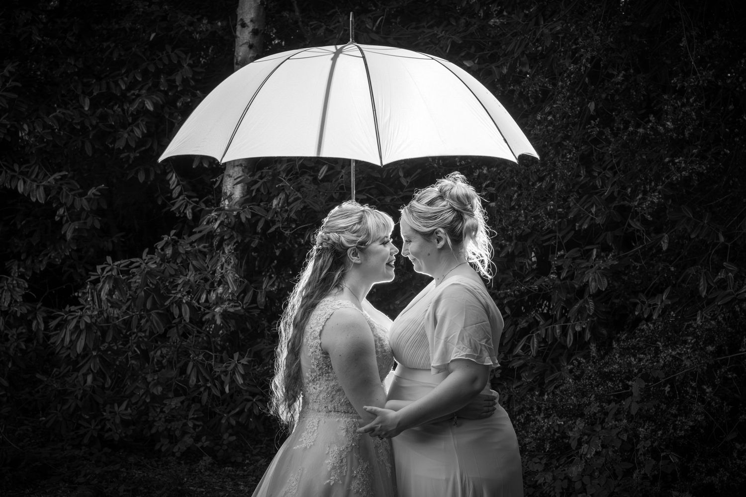 Artistic black and white wedding portraits with white umbrella creating silhouette effect.