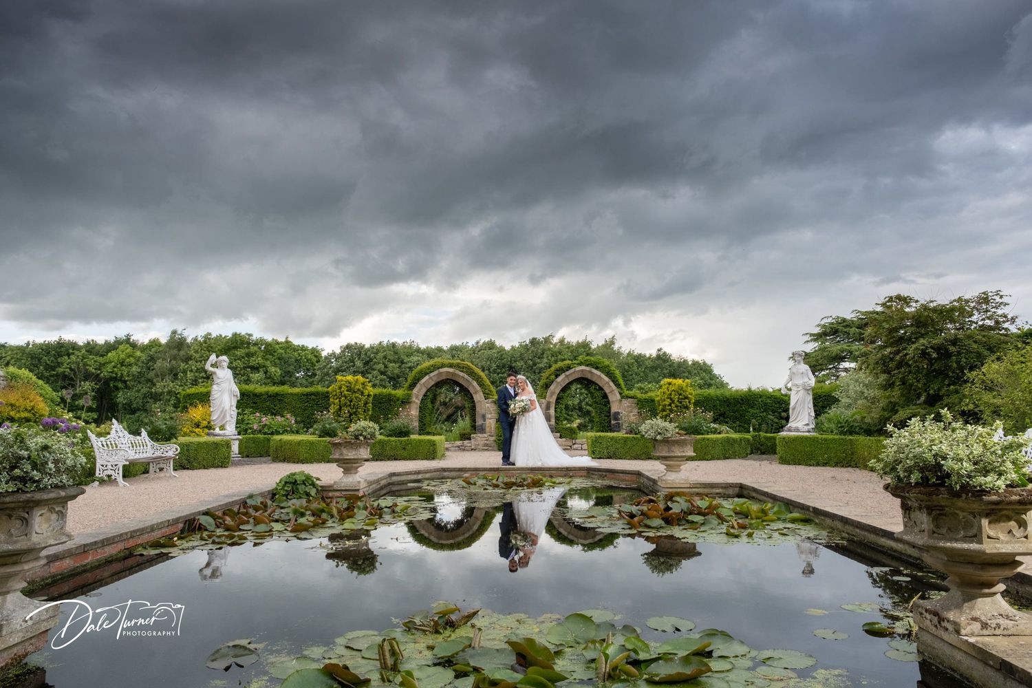 Dramatic cloudy sky over ornate garden wedding venue with reflecting pool.