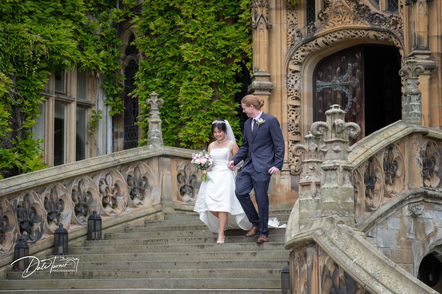 Wedding couple posing on ornate stone steps surrounded by gothic architecture.