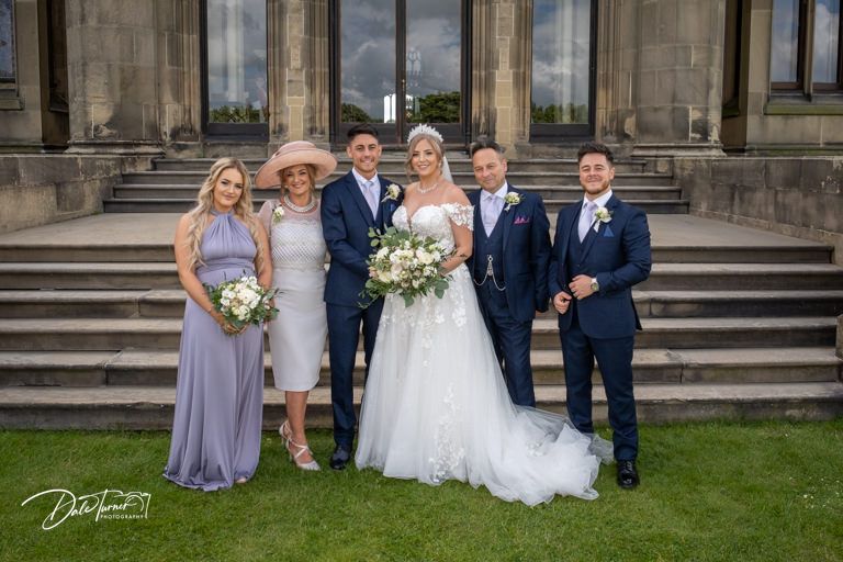 Wedding group portrait taken outside elegant stone building with classic architecture.