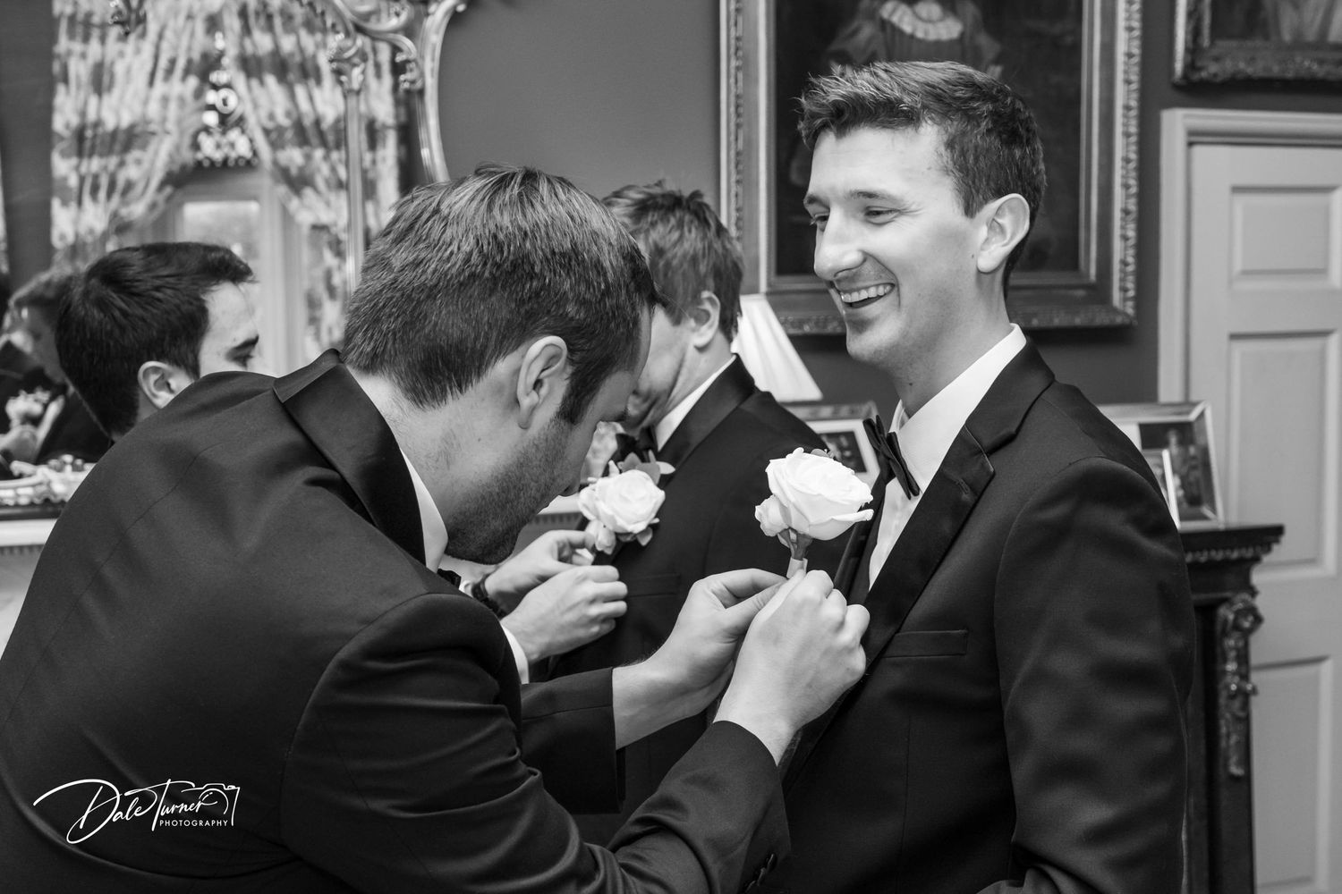 Wedding party shares candid laughs in formal black and white attire.