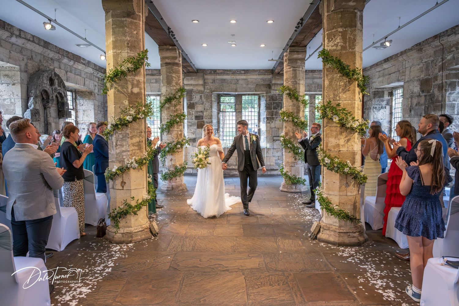 Wide view of wedding ceremony in rustic stone venue with guests seated.