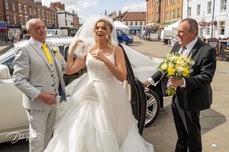 Wedding party gathering outside historic stone building on sunny day.