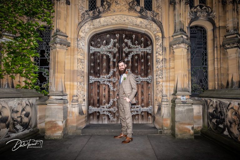 An elegant wedding portrait in front of an ornate Gothic doorway with intricate stone details.