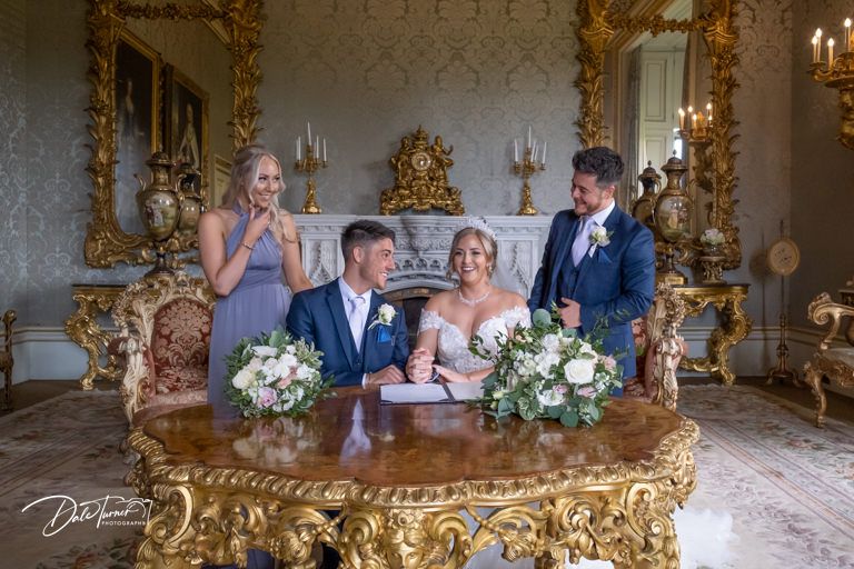 Wedding ceremony in an ornate gold-decorated room with elegant chandelier lighting.