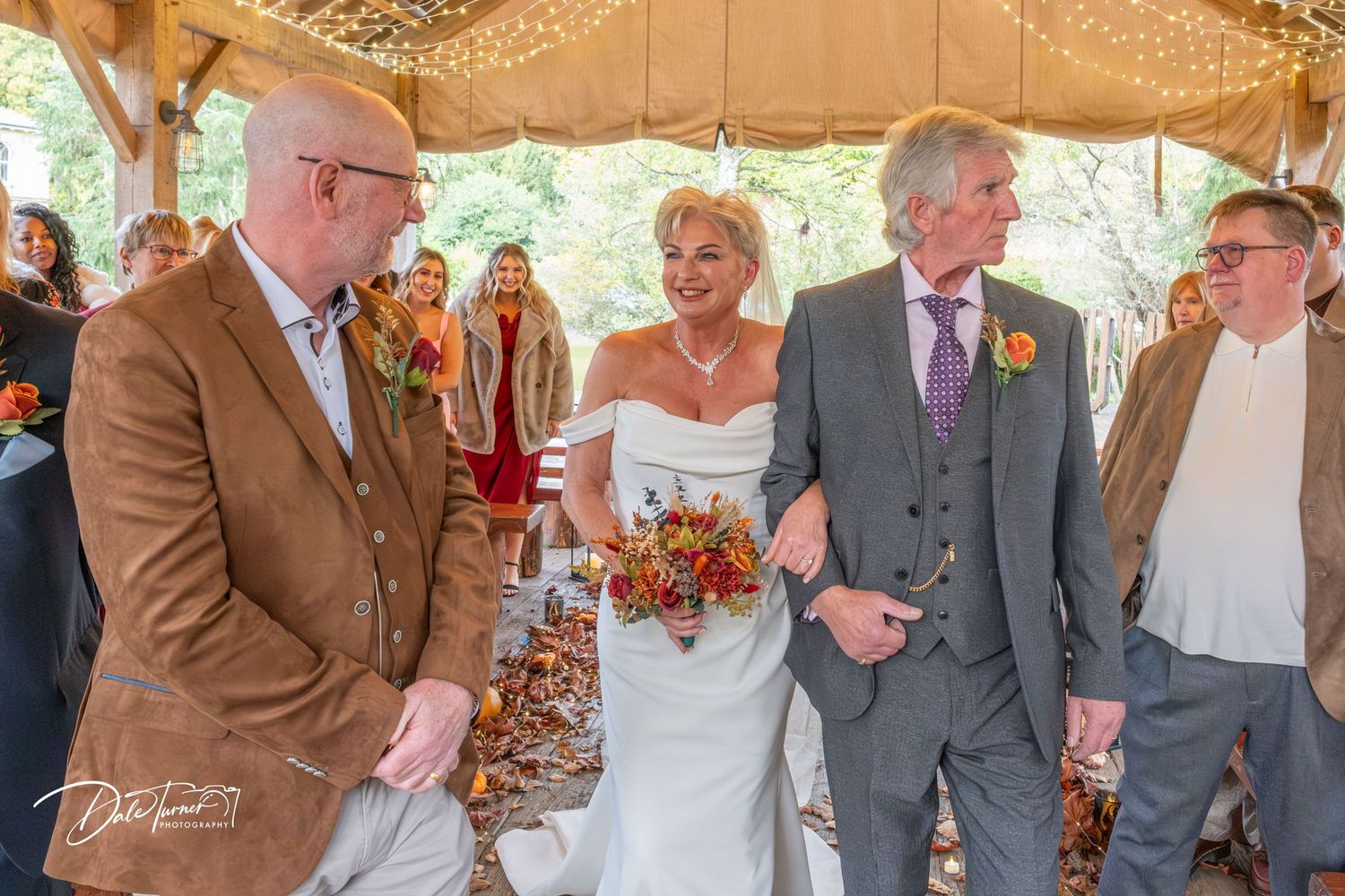 Outdoor wedding ceremony under a white tent with string lights and elegant decor.