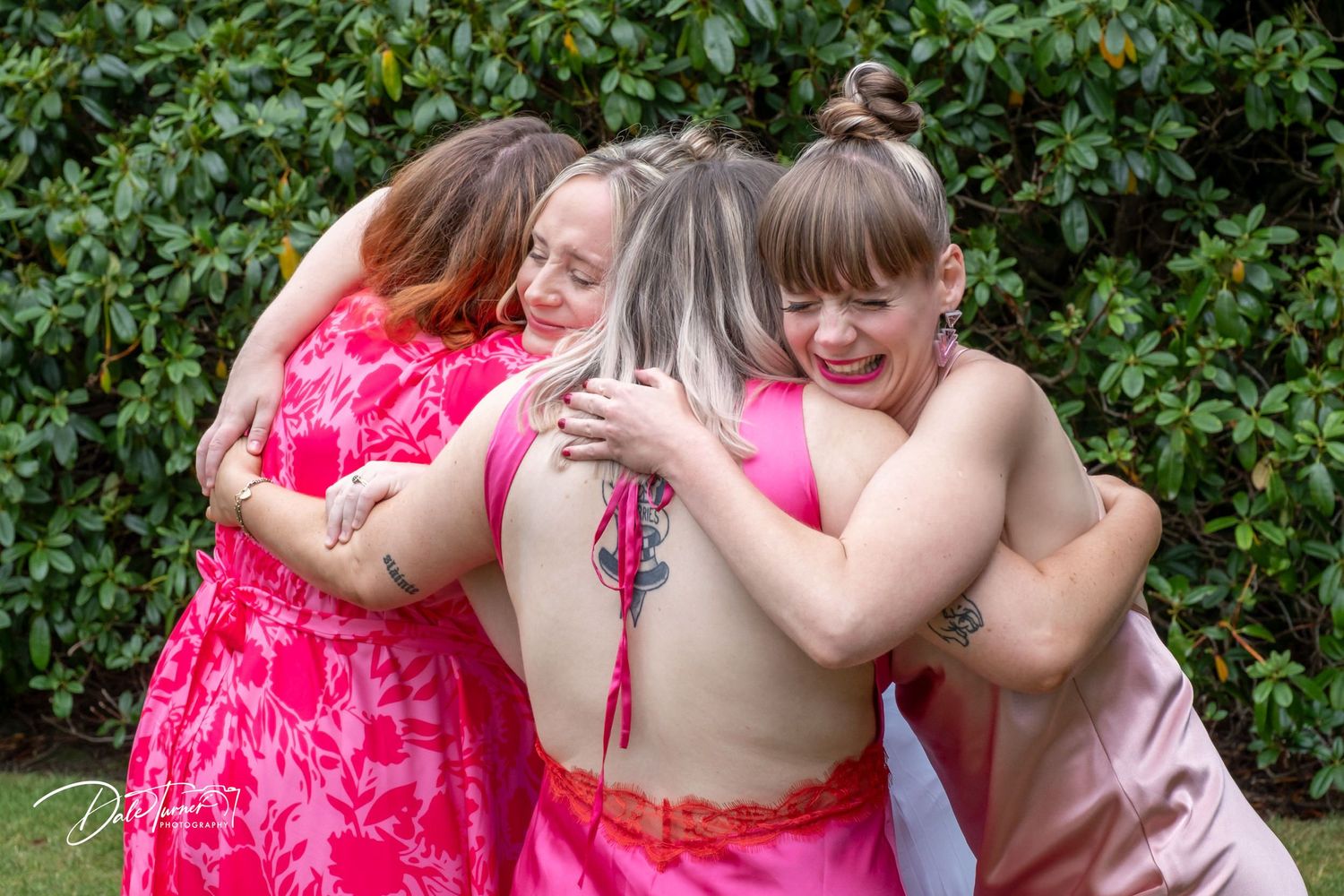Wedding attendees in bright pink and neutral dresses gather for group photos outdoors.
