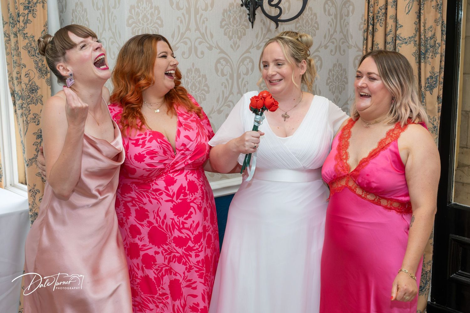 Wedding party members in pink and red dresses sharing joyful moments together.