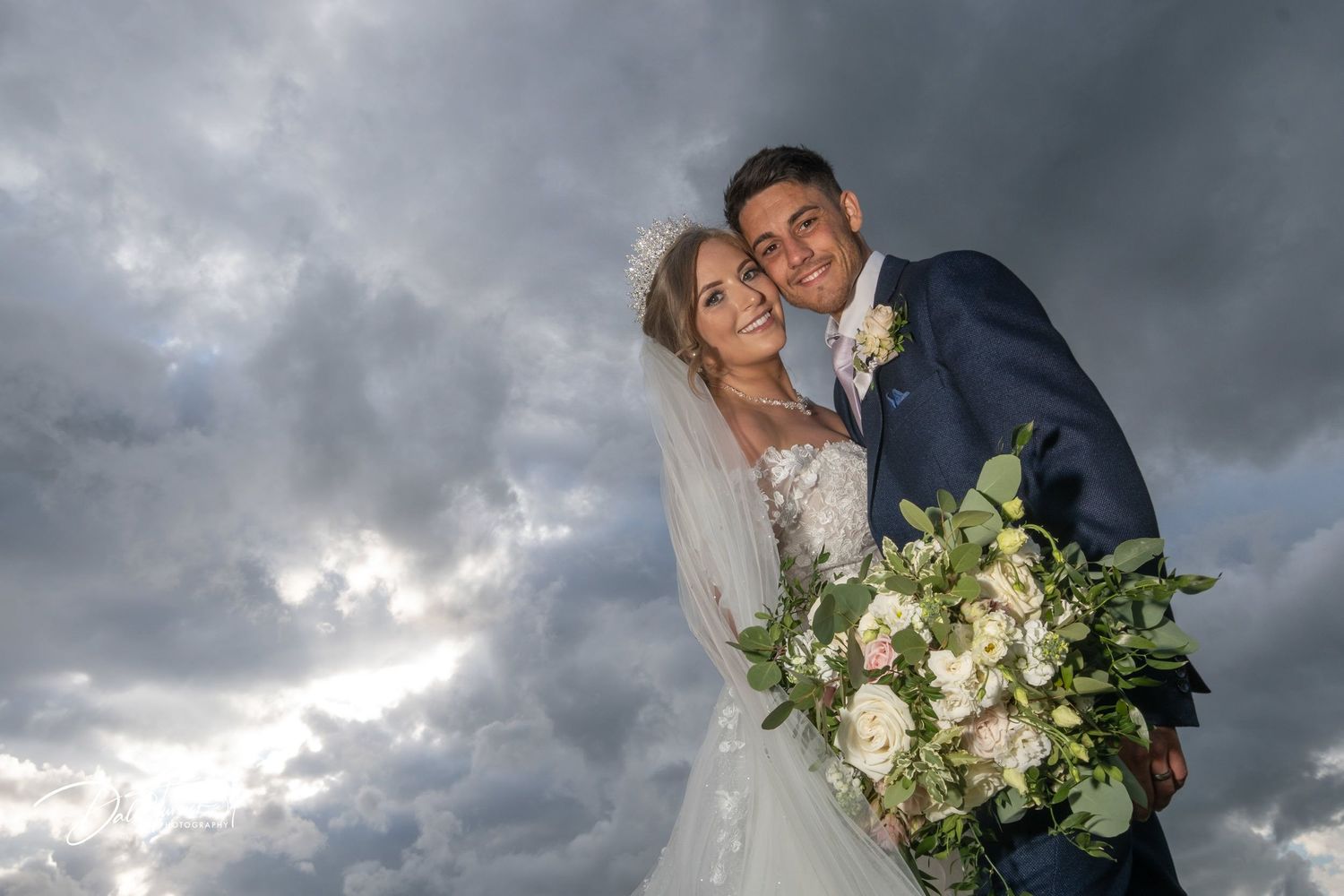 Romantic wedding portrait against dramatic stormy sky with natural lighting.