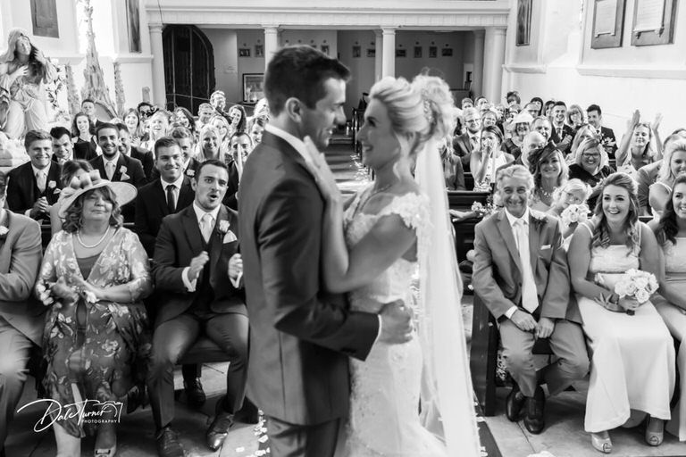 Wedding guests celebrate and applaud during an indoor reception ceremony.