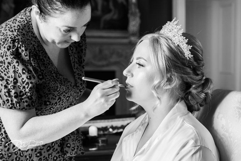 Wedding makeup application scene captured in black and white photography.