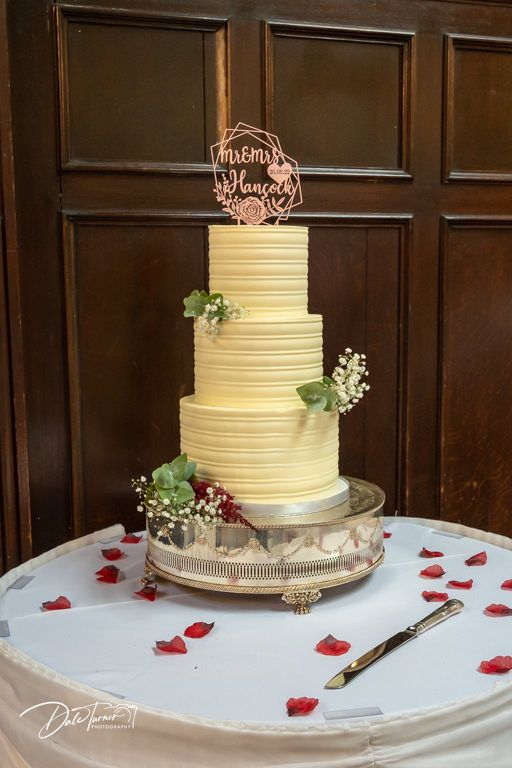 Elegant three-tiered white wedding cake with textured horizontal lines and delicate floral accents displayed on white tablecloth.