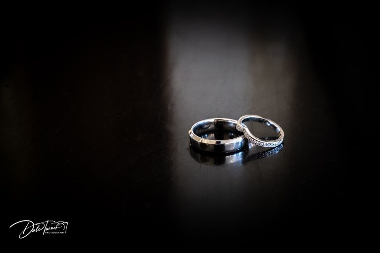 Artistic close-up of two wedding rings on dark background with dramatic lighting.