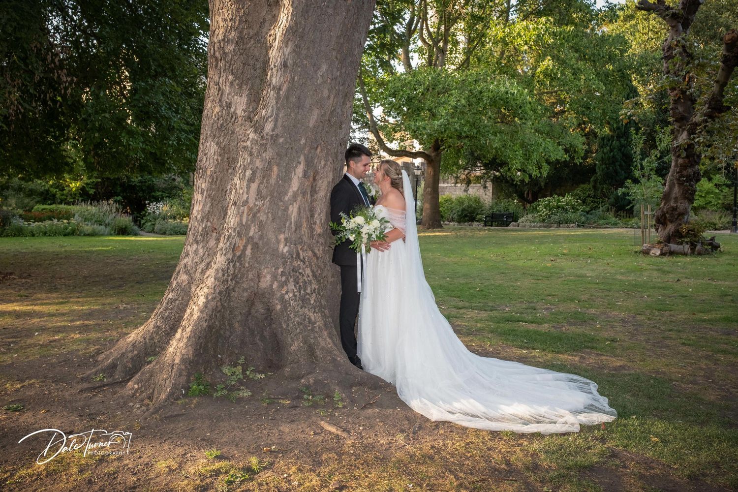 Wedding photography session in lush garden setting with dramatic train of white dress.