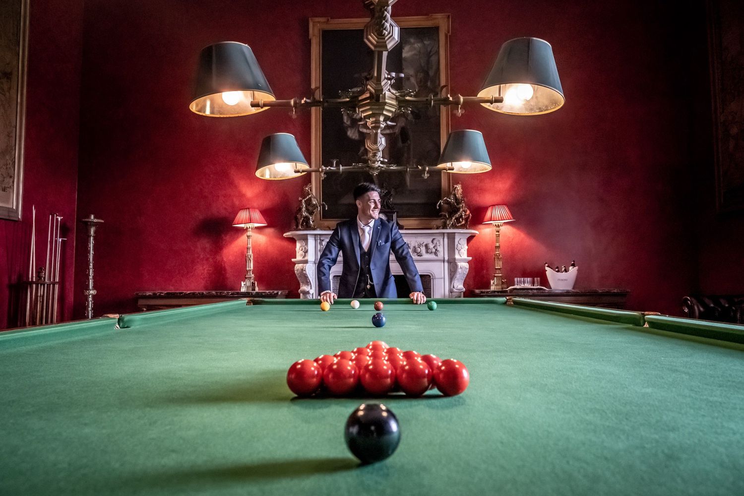Vintage snooker room with red walls and classic billiards table under pendant lighting.