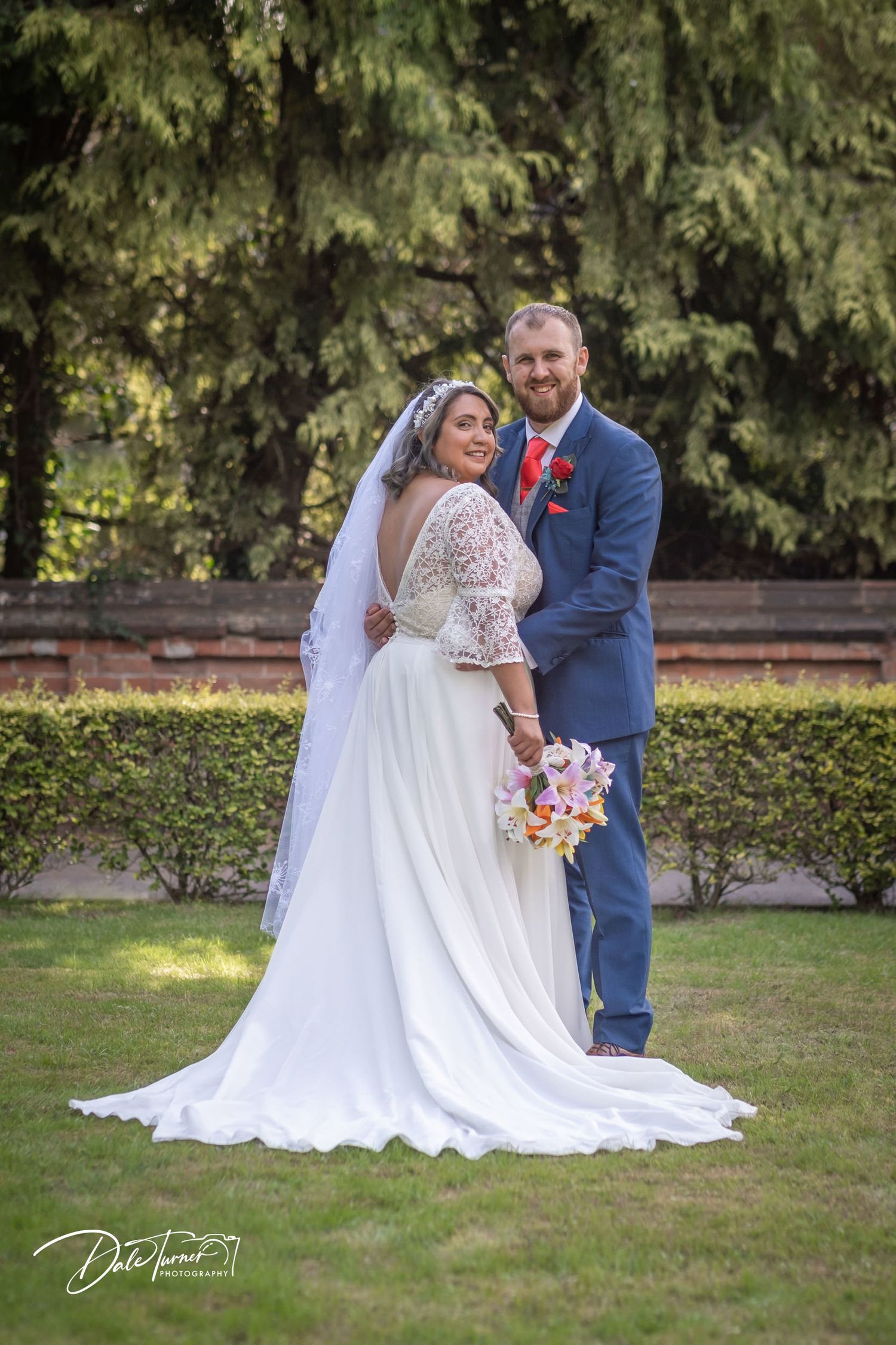 Wedding couple posing in garden setting with flowing white dress and bouquet.