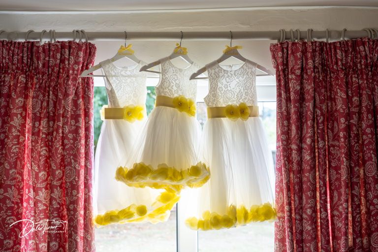 White wedding dresses with yellow petticoats hang on display against red curtains in a bridal preparation room.