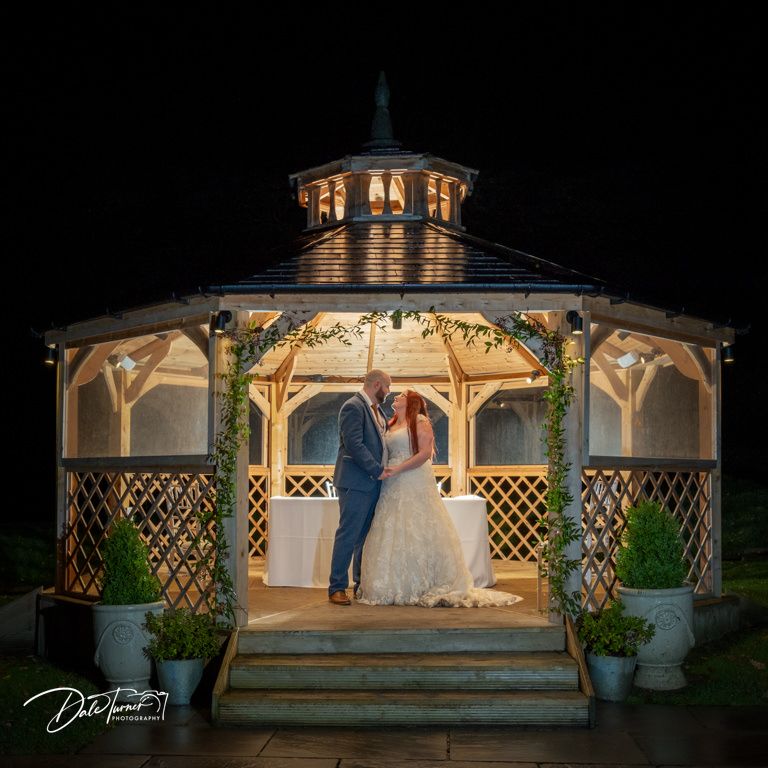 Illuminated wedding gazebo decorated with lattice and string lights creates a romantic evening ambiance.