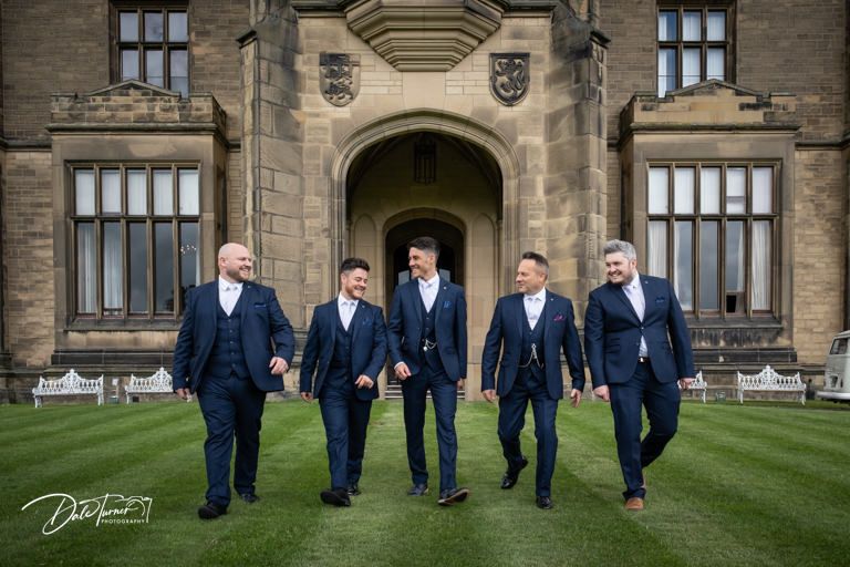 Groomsmen in navy suits posing together outside a grand stone building.