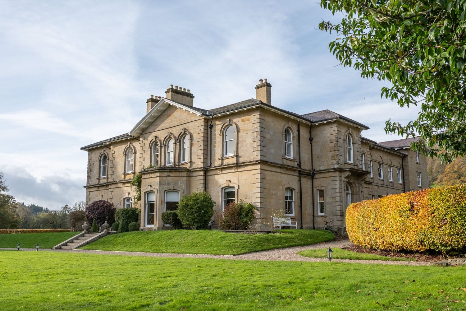 Panoramic view of a grand stone manor house with manicured lawn and gardens.