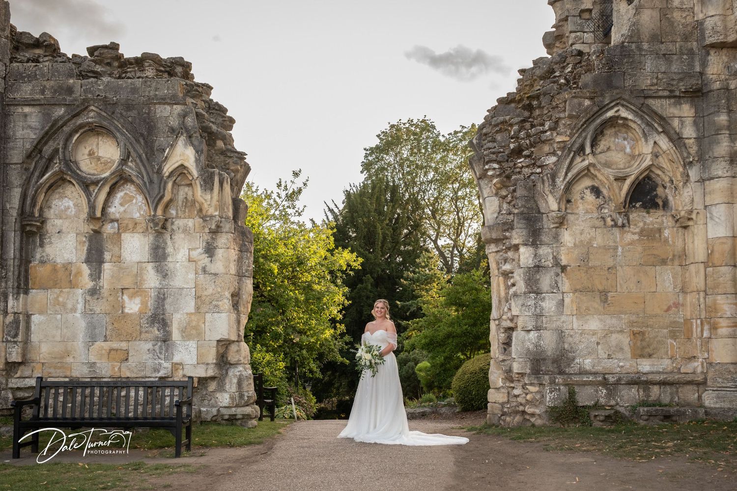 A wedding dress stands out against ancient stone ruins and gothic arches.