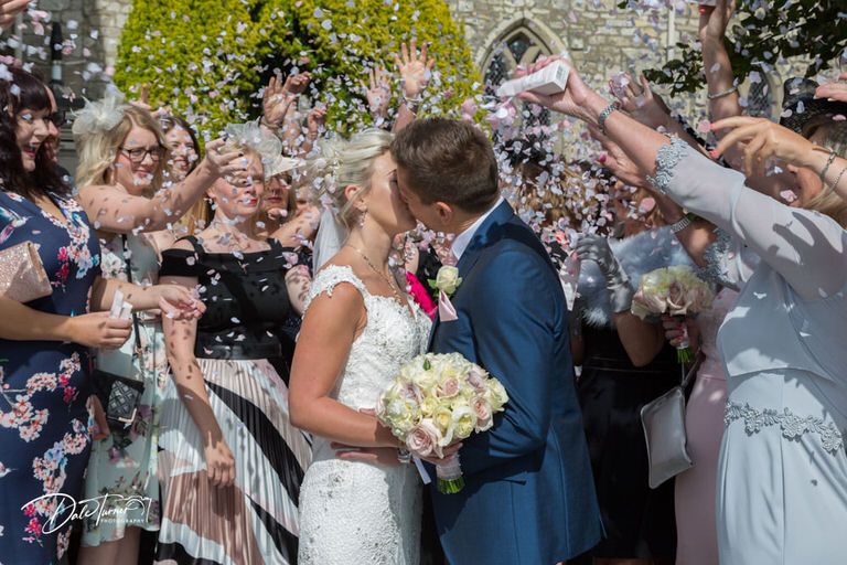 Wedding party celebrates with confetti toss outside in bright sunlight.