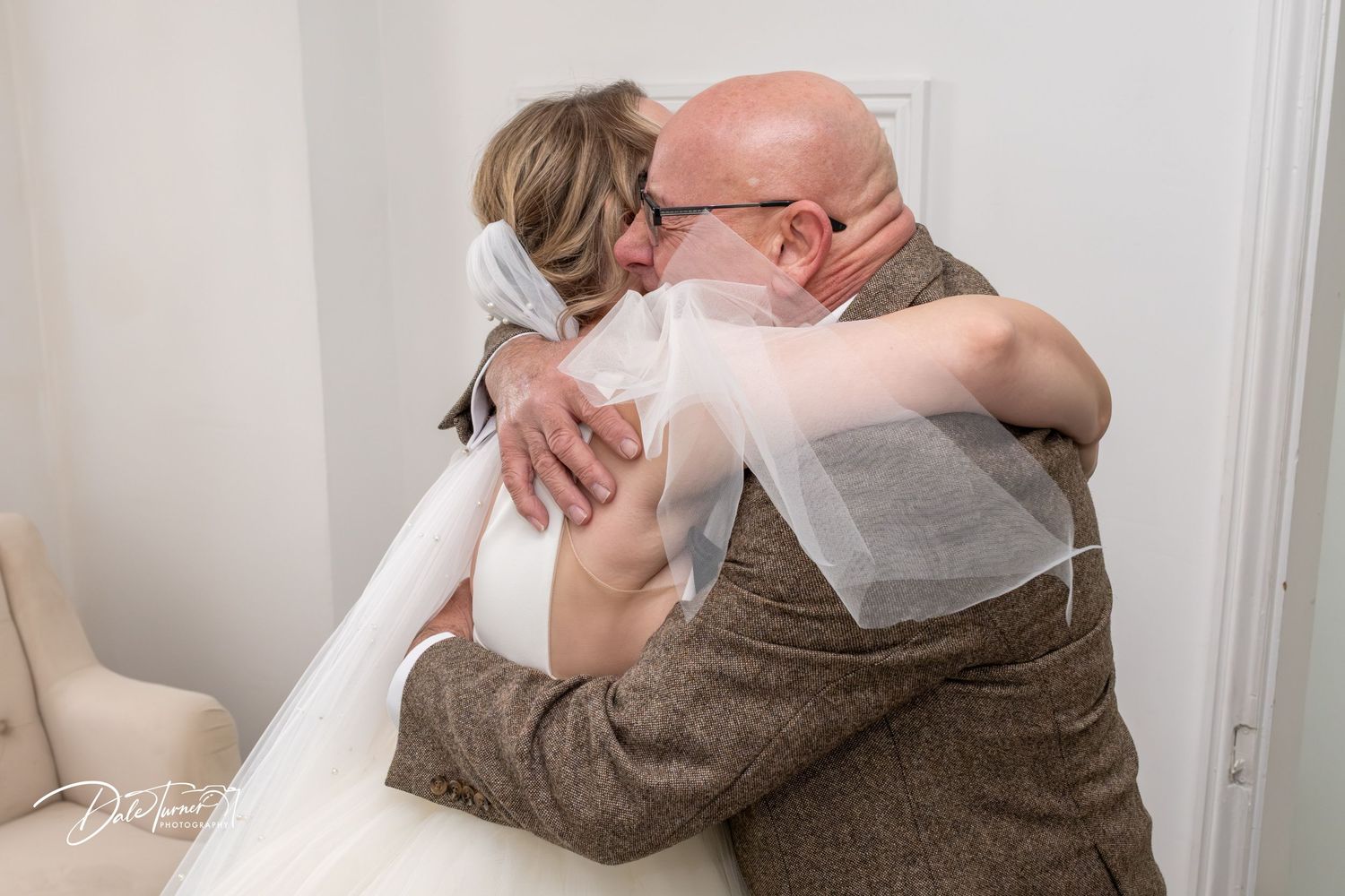 An emotional embrace between two people during what appears to be a wedding moment, with a white veil flowing.