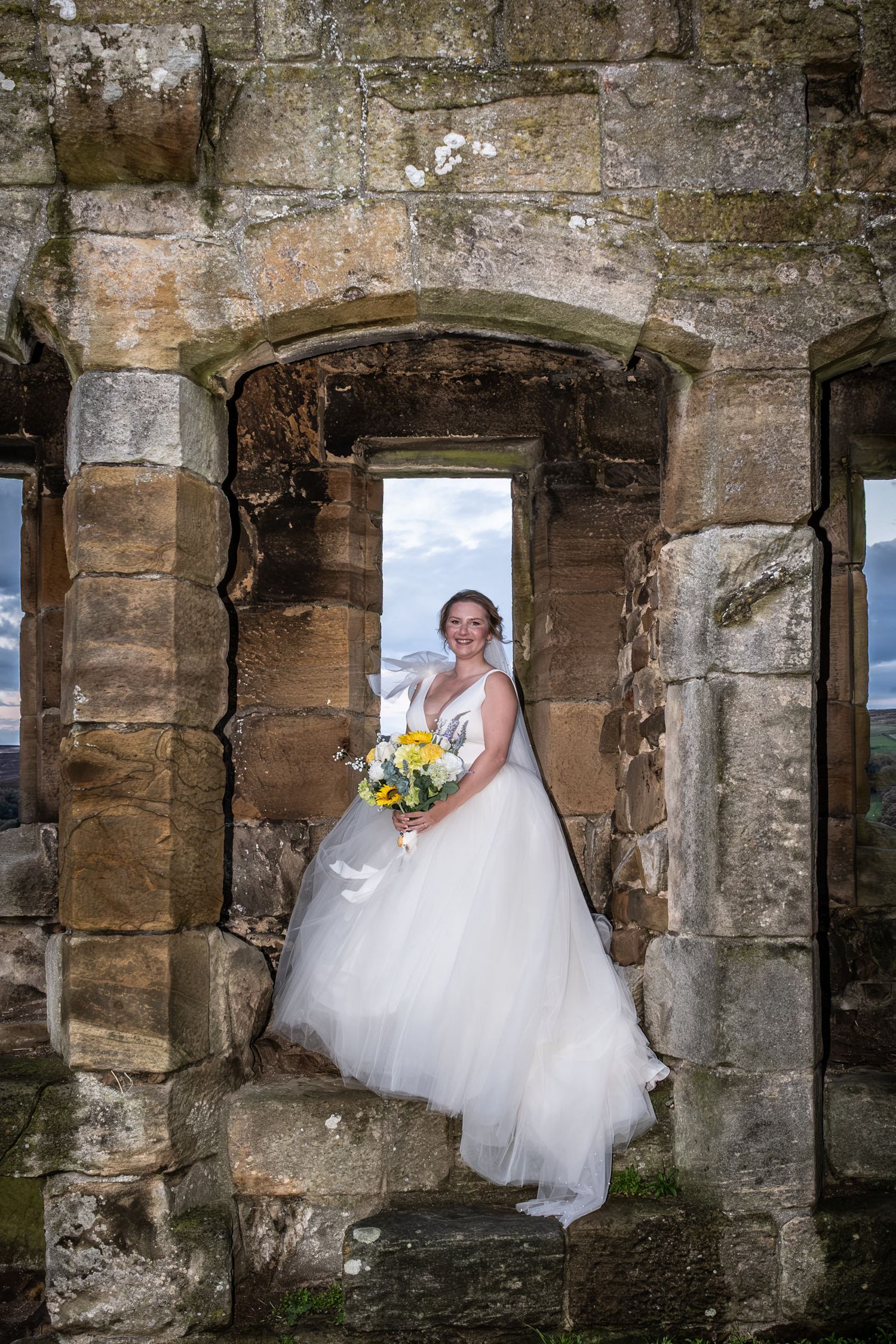 A bride in a white tulle gown poses in a series of stone archways at a historic venue.